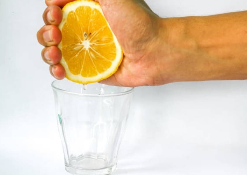 Mano exprimiendo medio limón sobre un vaso para preparar agua con limón.