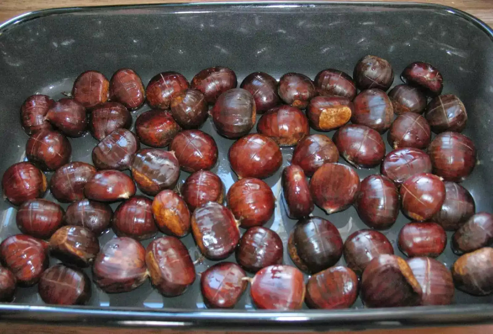 Castañas crudas con un corte en cruz sobre una bandeja de horno, listas para asar.
