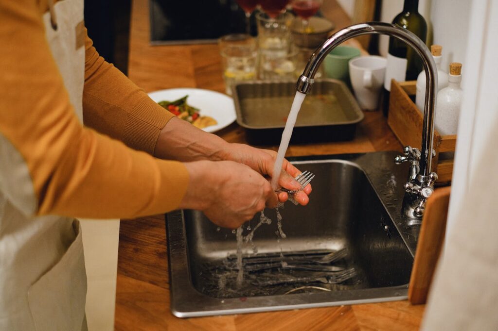 Persona lavando a mano utensilios de cocina variados en un fregadero.