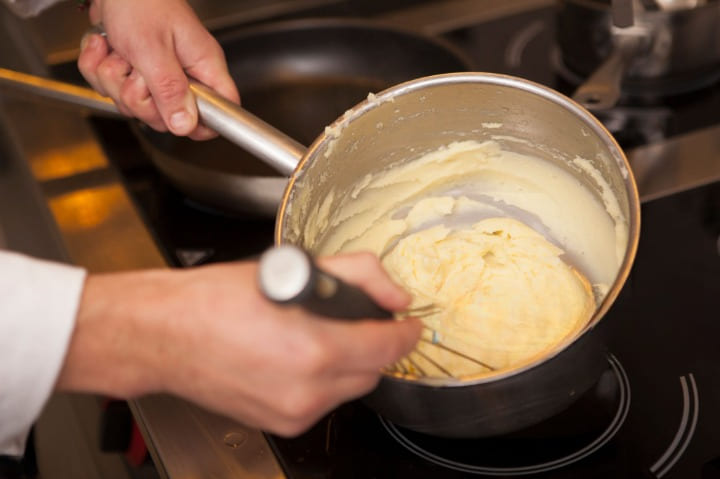 Bechamel cremosa para croquetas de jamón y queso espesándose en un cazo mientras se remueve con varillas.