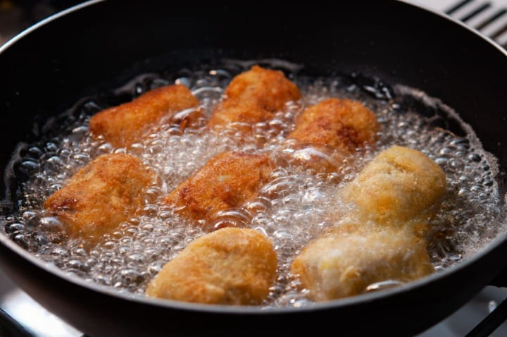 Croquetas dorándose en una sartén con abundante aceite caliente, mostrando el punto exacto de la fritura para que no se abran.
