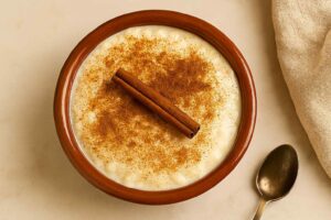 Cuenco de arroz con leche cremoso, espolvoreado con canela y decorado con una rama de canela.