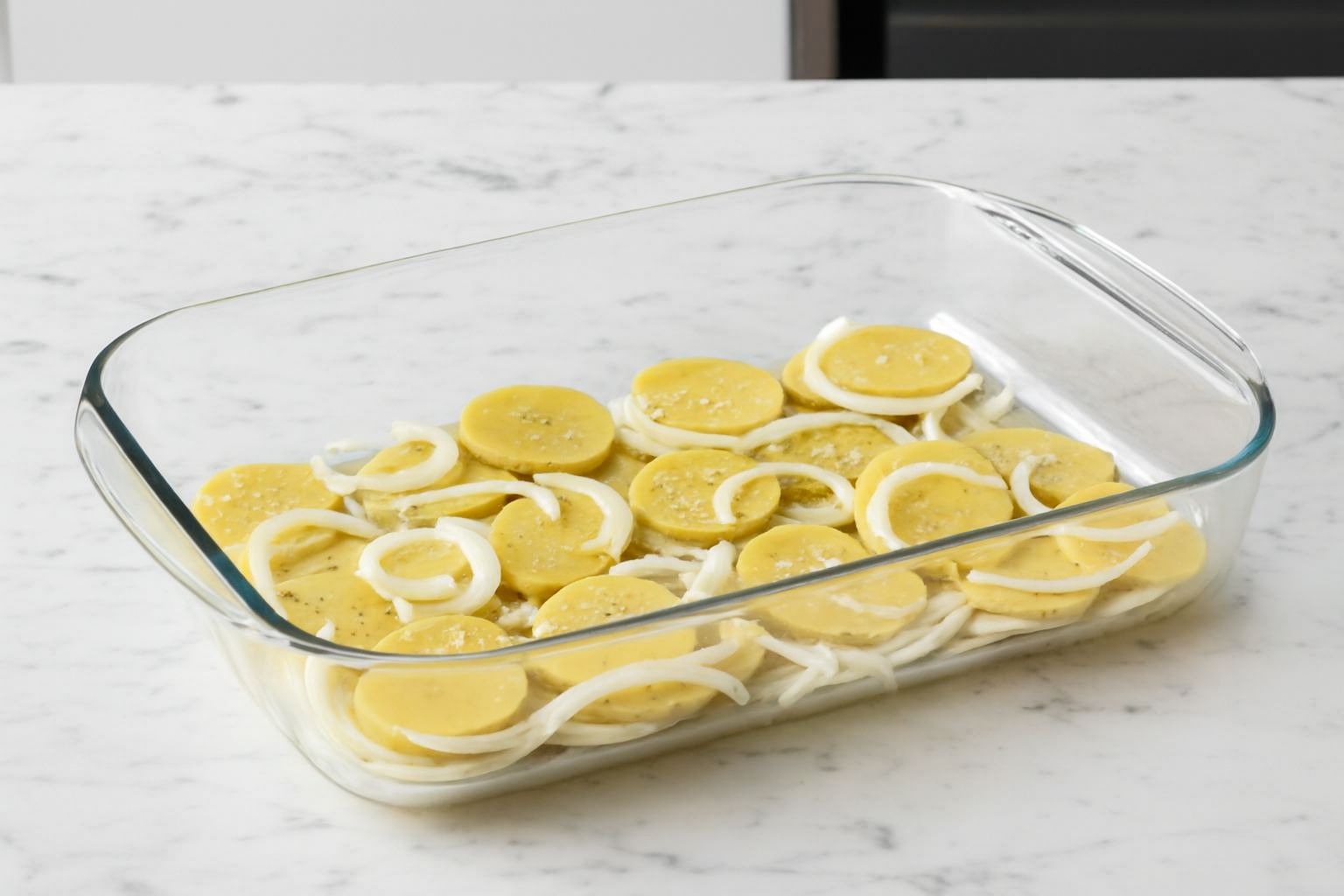 Bandeja de horno con patatas panadera y cebolla listas para hornear.