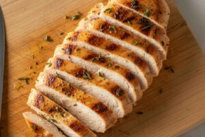 Pechuga de pollo a la plancha fileteada sobre una tabla de madera clara, mostrando su interior tierno y jugoso con especias y aceite de oliva.
