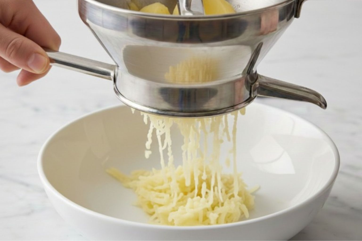 Técnica del pasapurés para un puré sin grumos Pasando los trozos de patatas cocidas por un pasapurés manual.